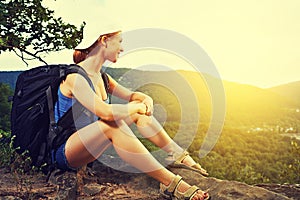 Woman tourist with a backpack sitting, resting on a mountain top on a rock on the journey