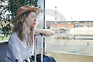 Woman tourist with baggage sits in the waiting room of the airport and she is sad