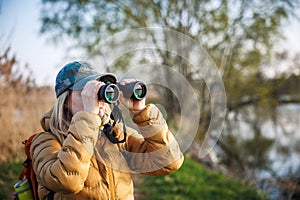 Woman tourist with binoculars looking for birds and animals at lake. Eco tourism