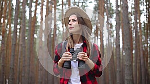 Woman tourist with binoculars looks around in the forest. Concept hike, tourism.