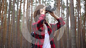 Woman tourist with binoculars looks around in the forest. Concept hike, tourism.