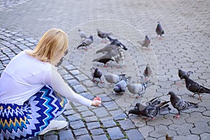 Woman tourist or citizen toss crumbs for pigeons. Girl blonde woman relaxing city square and feeding pigeons. Girl