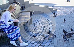 Woman tourist or citizen toss crumbs for pigeons. Group doves on city square waiting treats. Girl feeding dove birds