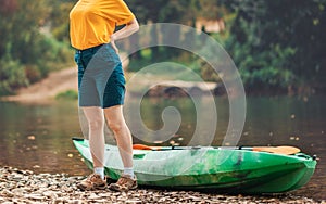 Woman in tourist clothes is standing near a kayak and holding her hands to the small of her back. Close up. Copy space