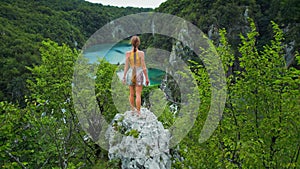 Woman tourist enjoying mountain view over lake with turquoise water and high waterfalls. Plitvice Lakes National Park in