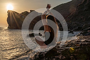 Woman tourist enjoying sunset over the sea mountain landscape. Sits outdoors on a rock above the sea. She is wearing