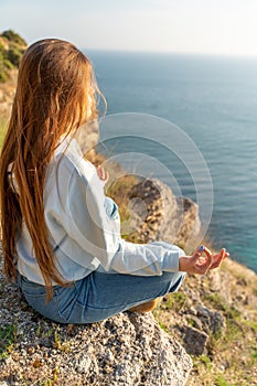 Woman tourist enjoying the sunset over the sea mountain landscape. Sits outdoors on a rock above the sea. She is wearing