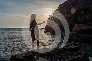 Woman tourist enjoying the sunset over the sea mountain landscape. Sits outdoors on a rock above the sea. She is wearing