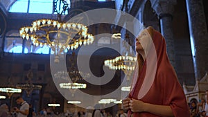 A woman tourist, her head draped in a scarf, stands in awe within the hallowed beauty of Istanbul's Ayasofya