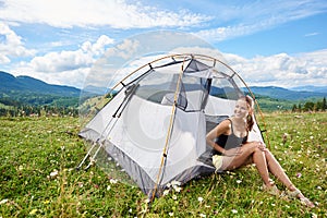 Woman tourist hiking in mountain trail, enjoying summer sunny morning in mountains near tent