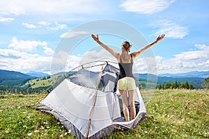 Woman tourist hiking in mountain trail, enjoying summer sunny morning in mountains near tent