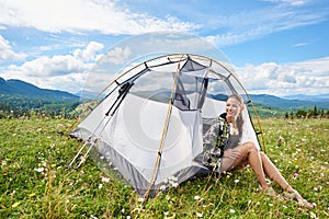 Woman tourist hiking in mountain trail, enjoying summer sunny morning in mountains near tent