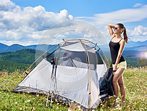 Woman tourist hiking in mountain trail, enjoying summer sunny morning in mountains near tent