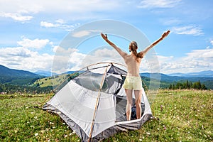 Woman tourist hiking in mountain trail, enjoying summer sunny morning in mountains near tent