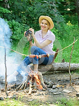 Woman tourist holds binoculars while sits on log near bonfire. Observing nature concept. Girl ornithology expedition in