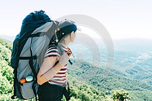 A woman tourist with a large camping backpack on an expedition stands on top and looks at the landscape.