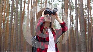 Woman tourist looks through binoculars in the forest. Concept hike, tourism.