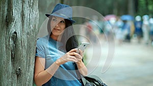 Woman tourist with mobile phone texting sms in the park in warm spring day.