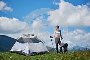 Woman tourist near camping in the mountains with backpack and trekking sticks in the morning