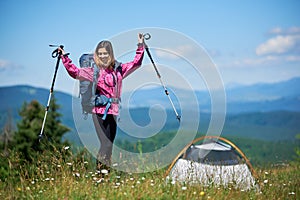 Woman tourist near camping in the mountains with backpack and trekking sticks in the morning