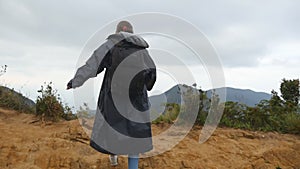 Woman tourist in raincoat running to the edge of beautiful canyon, victoriously outstretching arms up. Young female