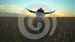Woman tourist running in wheat field at summer sunset. Hiker traveler woman in hat with backpack hikking in nature. Girl