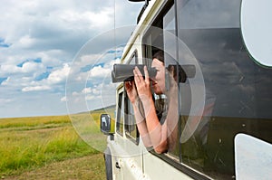 Woman tourist on safari in Africa, travel in Kenya, watching wildlife in savanna with binoculars