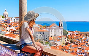 Woman tourist sitting on balcony looking at panoramic view of rooftop of Lisbon