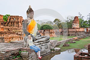 Woman tourist sitting under buddha statue in Ayutthaya