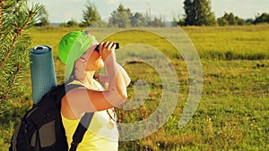 A woman tourist stands in a forest glade and looks through binoculars where to go next