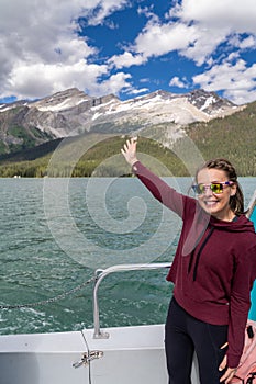 Woman tourist stands on the Spirit Island boat cruise on Maligne Lake with an arm up in the air, enjoying the ride