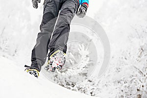 Woman tourist on a trail in snowy mountains. Crampons on shoes.