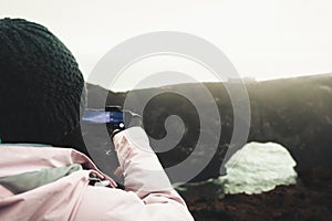 Woman tourist visit sightseeing Dyrholaey landmark hold smart phone photograph capture natural wonders in Iceland to post on