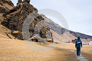 Woman Tourist visit turf house and Drangurinn Rock in Southern Iceland. Eyjafjll mountains near Ring Road, Route 1. Turfhouses