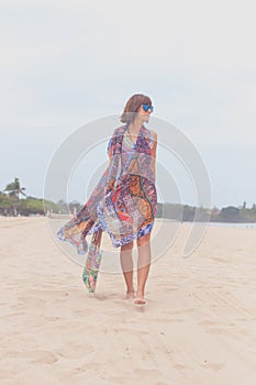 Woman tourist walking on a tropical summer vacation beach wearing sunglasses and beach bag relaxing on travel holidays