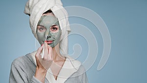 Woman with a towel on her head applies cream to her face.