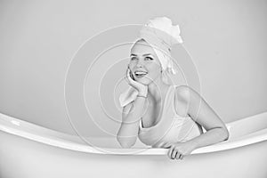 Woman with towel turban sitting in white bathtub