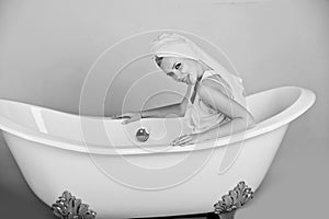 Woman with towel turban sitting in white bathtub