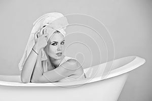 Woman with towel turban sitting in white bathtub