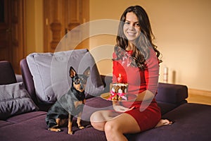 Woman and toy terrier with dog cake on sofa