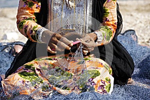 Woman in traditional dress mending fishing net, Oman photo