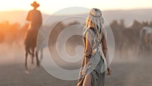 Woman in traditional Indian western dress on the background of herd of horses and cowboy