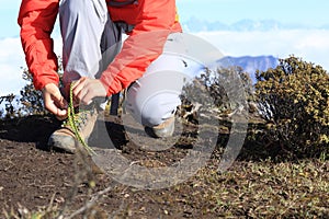 Woman trail runner tying shoelace on mountain peak