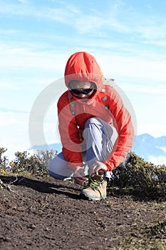 Woman trail runner tying shoelace on mountain peak