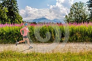 Woman trail running on country road in mountains, summer day