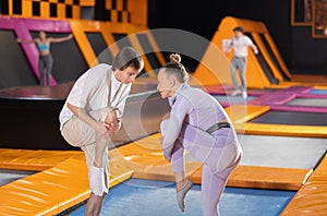 Woman trainer instructing young man doing exercises in trampoline arena