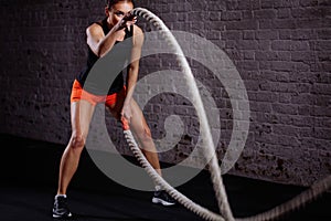 Woman training with battle rope in cross fit gym