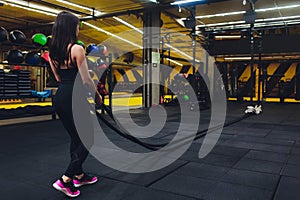 Woman training with battle ropes in gym, doing intense hard training.