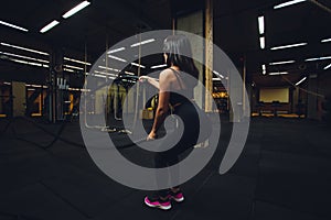 Woman training with battle ropes in gym, doing intense hard training.