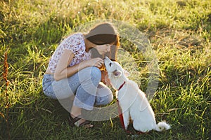 Woman training cute white puppy to behave and caressing him in summer meadow in warm sunset light. Adorable fluffy puppy  kissing photo